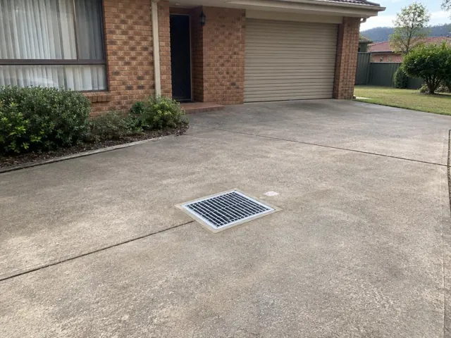 Concrete driveway with a clean metal drain grate beside a brick house in Chisholm