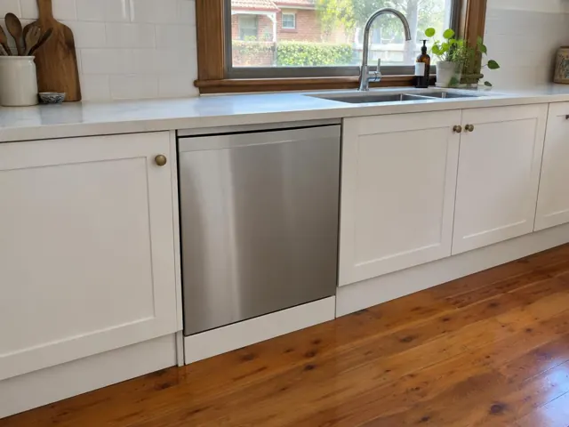 Stainless dishwasher built into white kitchen cabinetry under a window with timber trim in Morpeth