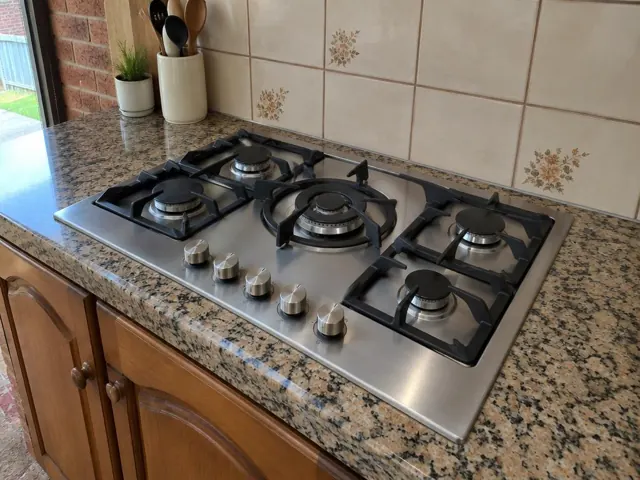 Stainless steel gas cooktop set into a speckled stone benchtop with tiled splashback in Metford
