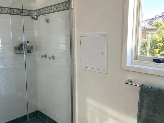 Bathroom wall with a small access panel beside a shower and window in Berry Park